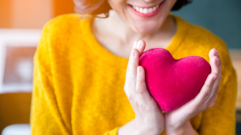smiling woman holding a bright pink heart