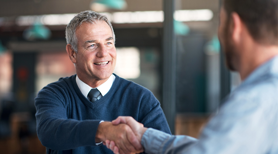 A senior, white, male hiring manager shaking hands with a young, bearded, male candidate, and feeling confident in his hiring decision because of MCode's Job Fit Report